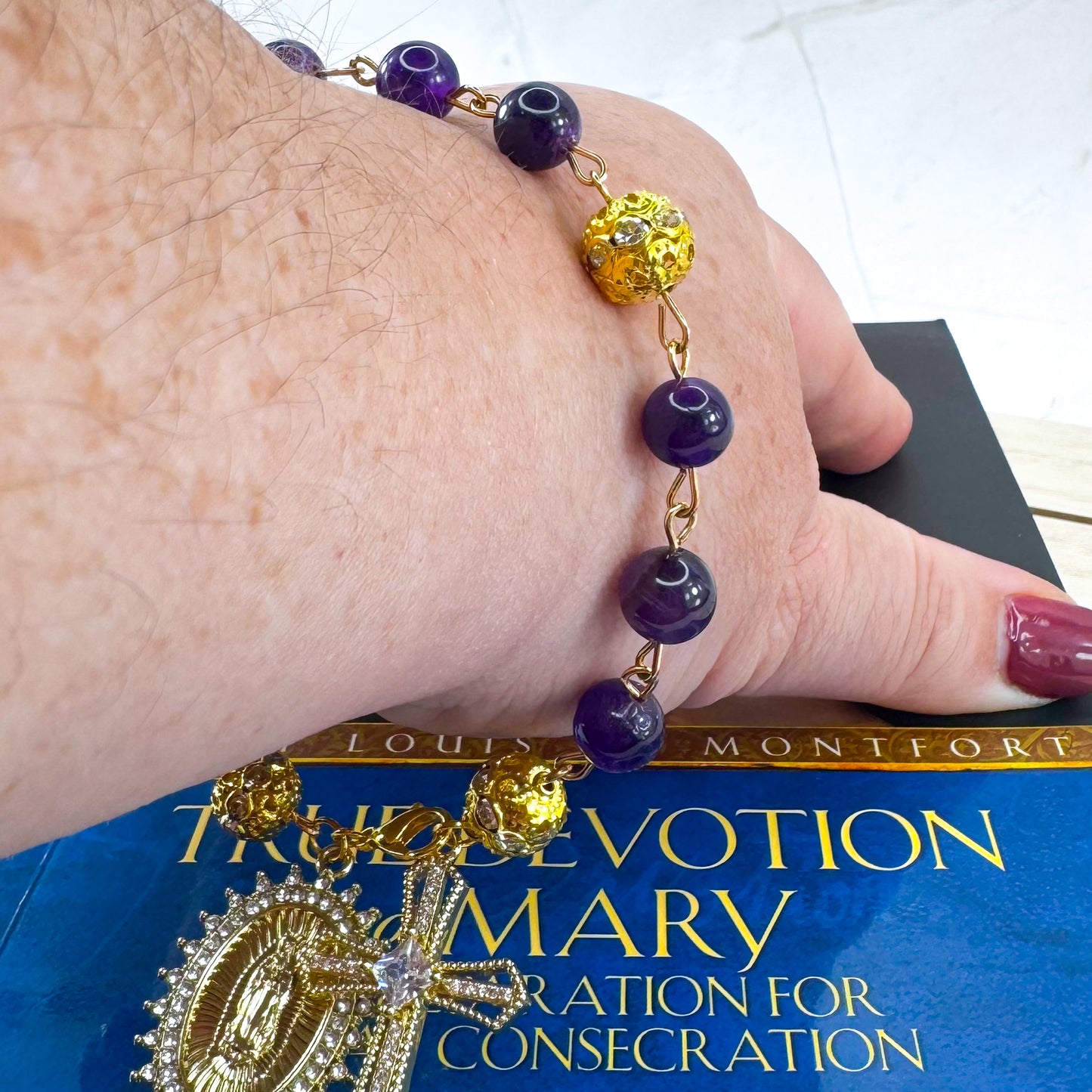 Handmade Catholic rosary bracelet with amethyst beads, sparkling gold cross, and Our Lady of Guadalupe medal. Perfect for gifts or prayer. Made in Edmonton, AB, Canada.