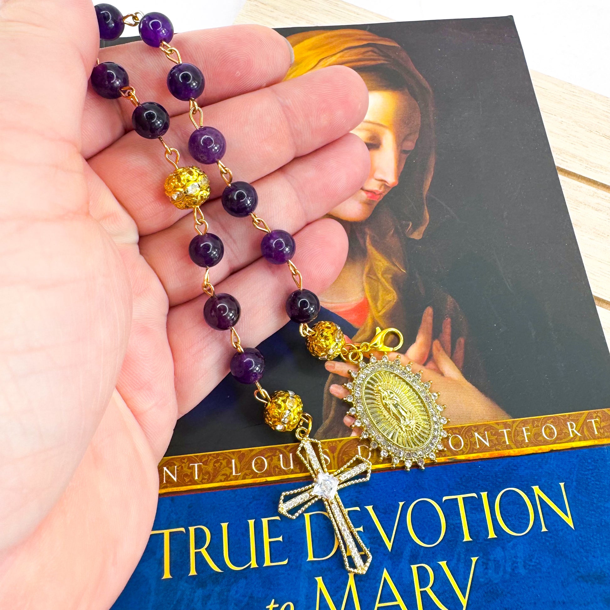 Handmade Catholic rosary bracelet with amethyst beads, sparkling gold cross, and Our Lady of Guadalupe medal. Perfect for gifts or prayer. Made in Edmonton, AB, Canada.