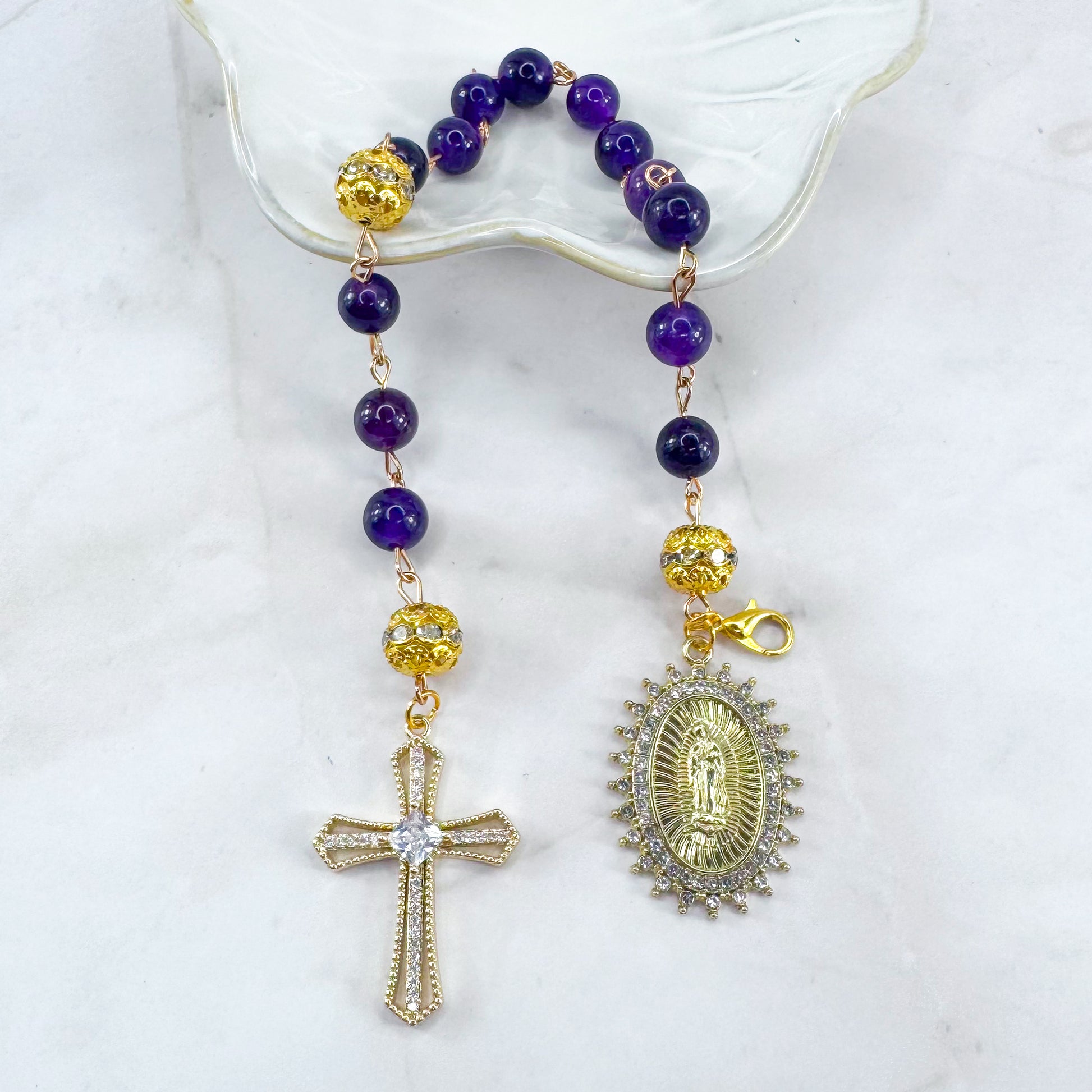 Handmade Catholic rosary bracelet with amethyst beads, sparkling gold cross, and Our Lady of Guadalupe medal. Perfect for gifts or prayer. Made in Edmonton, AB, Canada.