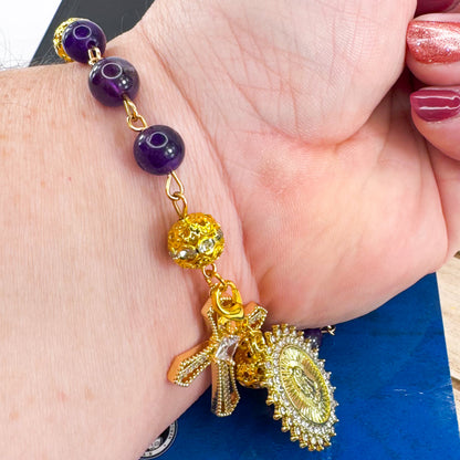 Handmade Catholic rosary bracelet with amethyst beads, sparkling gold cross, and Our Lady of Guadalupe medal. Perfect for gifts or prayer. Made in Edmonton, AB, Canada.